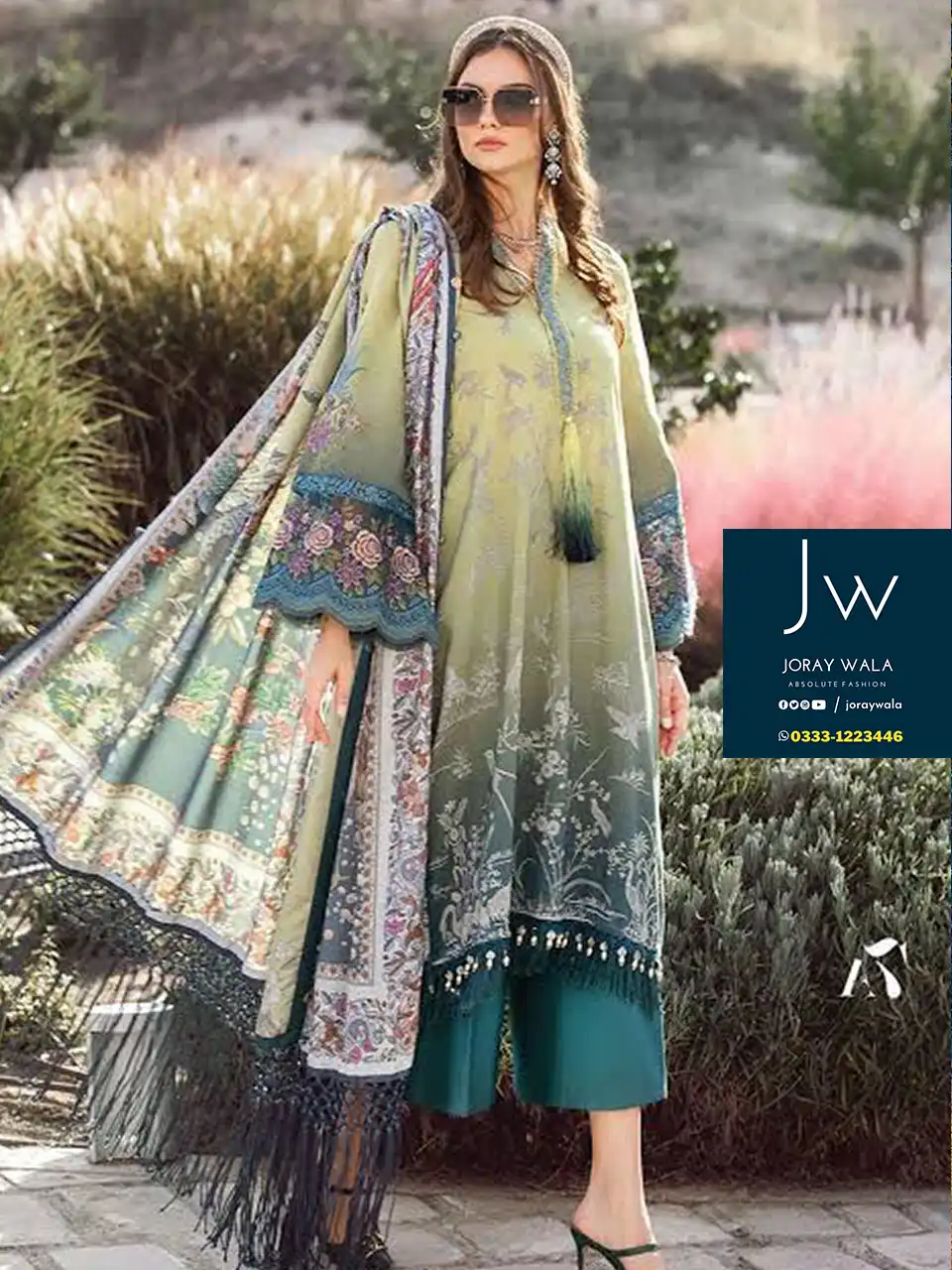 Model wearing a maria b Luxury lawn collection suit and standing in a garden, the suit has a beautiful combination of seagreen and green color