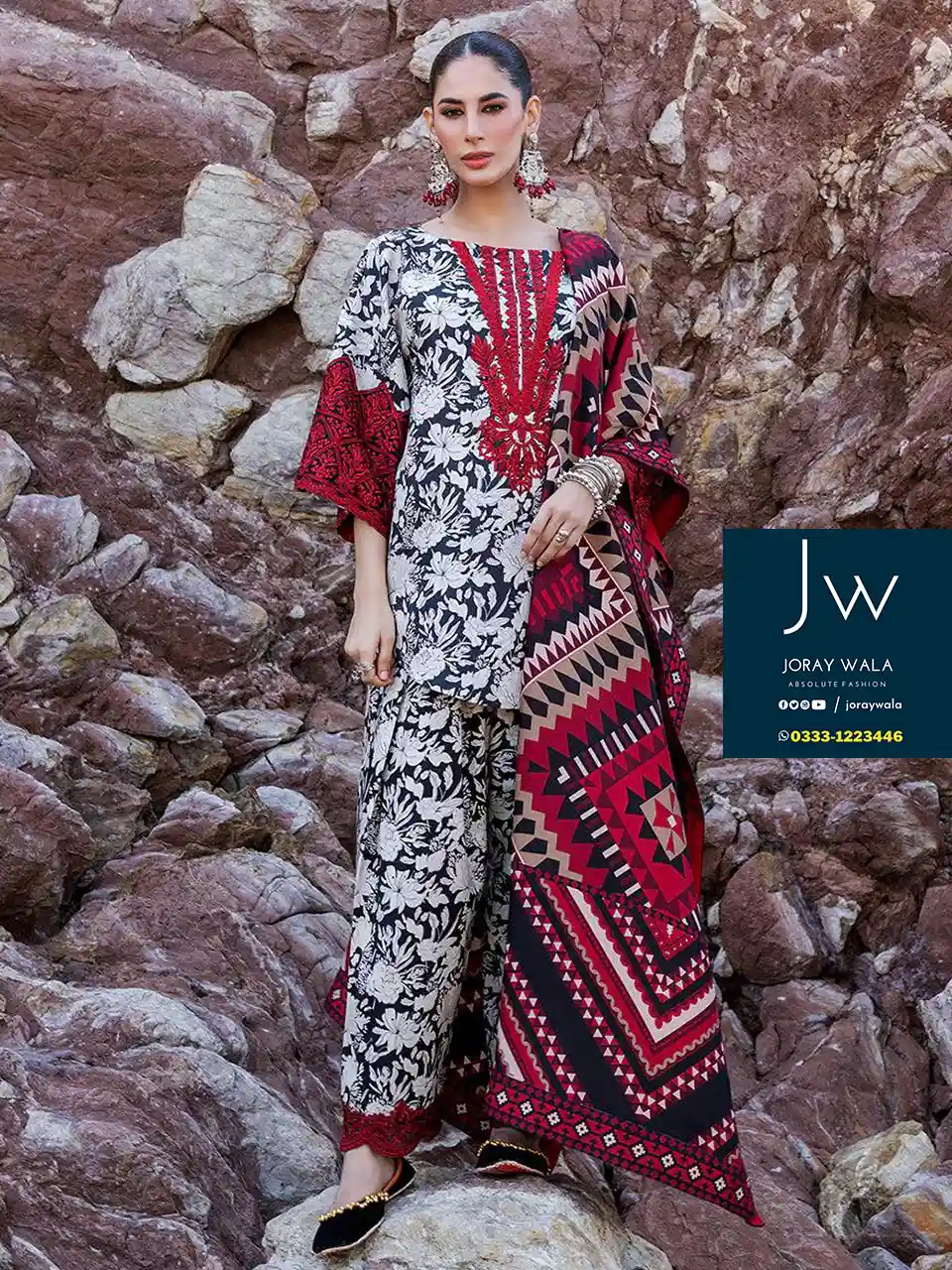 Bright sunny day and the model wearing zainab chottani stunning collection and standing at the sea, with rock. the suit have floral print.