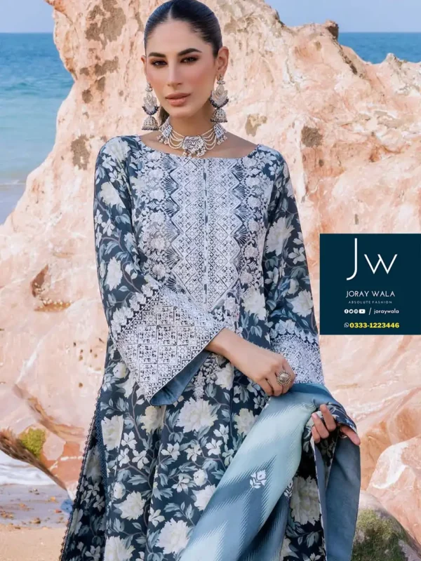 Bright sunny day and the model wearing zainab chottani stunning collection and standing at the sea, with rock. the suit have floral print.